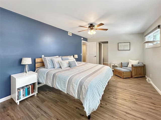 bedroom featuring a ceiling fan, visible vents, baseboards, and wood finished floors