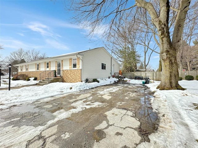 view of snow covered exterior with brick siding and fence