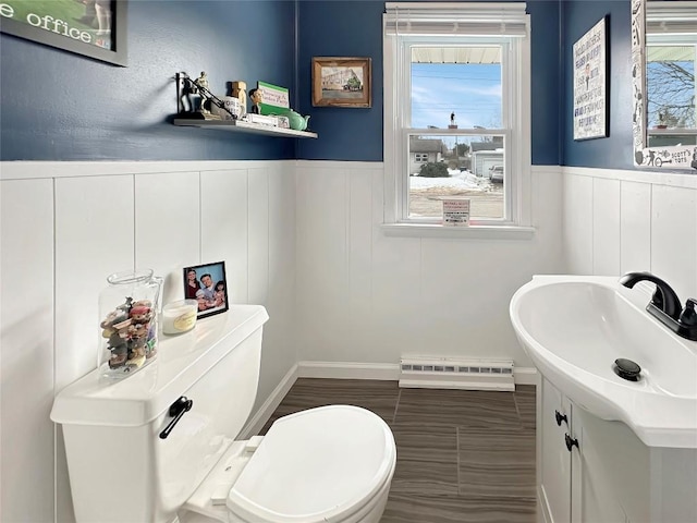 bathroom with a baseboard radiator, wainscoting, vanity, and toilet