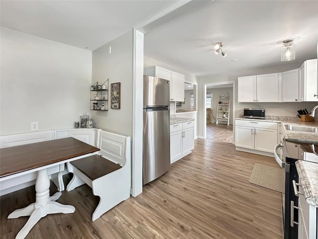 kitchen featuring stainless steel appliances, a sink, white cabinets, light wood-type flooring, and light stone countertops