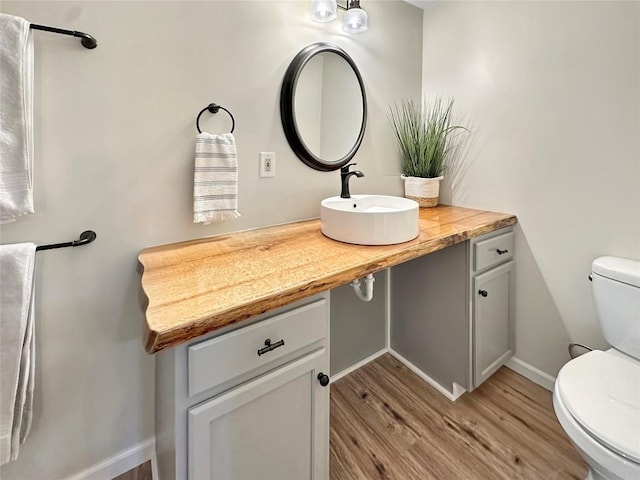 half bathroom featuring toilet, baseboards, a sink, and wood finished floors