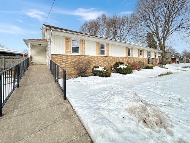 view of snow covered exterior featuring driveway, fence, a carport, and brick siding