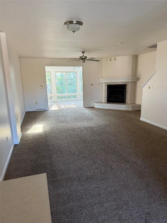 unfurnished living room featuring ceiling fan, carpet floors, and a tiled fireplace