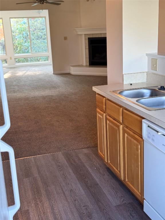 kitchen with dishwasher, sink, ceiling fan, a fireplace, and dark hardwood / wood-style flooring