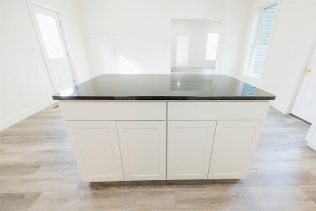 kitchen with a center island, light hardwood / wood-style flooring, white cabinetry, and dark stone countertops