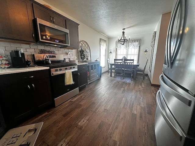 kitchen with dark wood-style flooring, decorative backsplash, a chandelier, stainless steel appliances, and light countertops