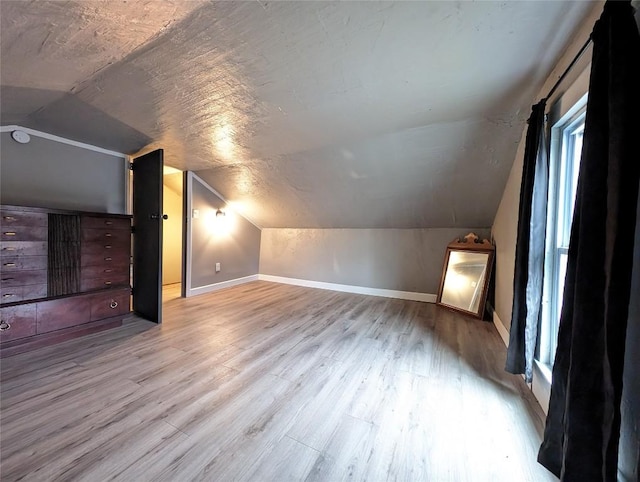 bonus room featuring a textured ceiling, light wood-type flooring, and lofted ceiling