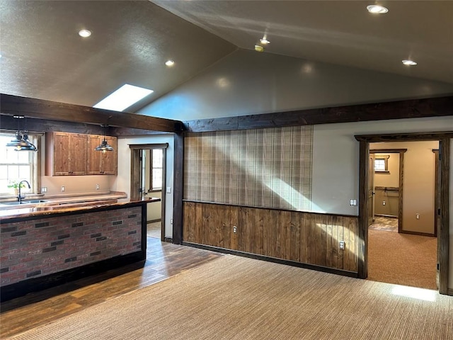 kitchen featuring sink, wood walls, lofted ceiling with skylight, light colored carpet, and decorative light fixtures