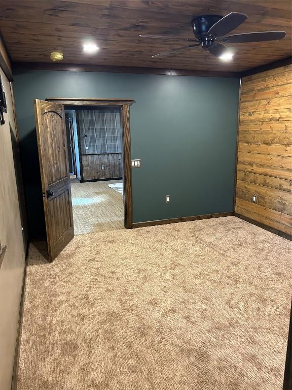 spare room featuring ceiling fan, wood ceiling, light carpet, and wooden walls