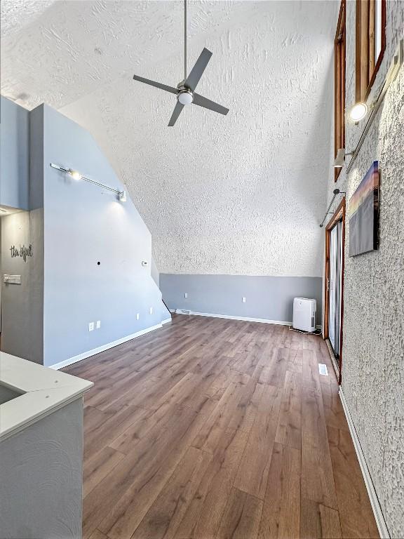 unfurnished living room featuring dark wood-type flooring, ceiling fan, lofted ceiling, and a textured ceiling