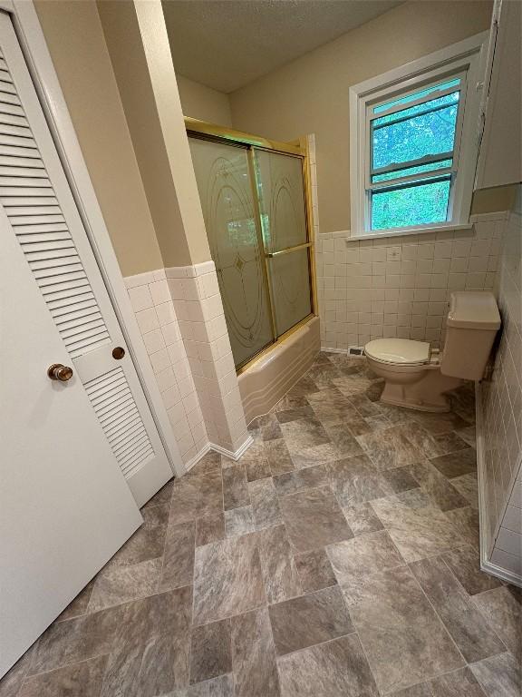 3322 Patio Dr, Millcreek, PA 16506 - full bath with tile walls, toilet, bath / shower combo with glass door, and a wainscoted wall