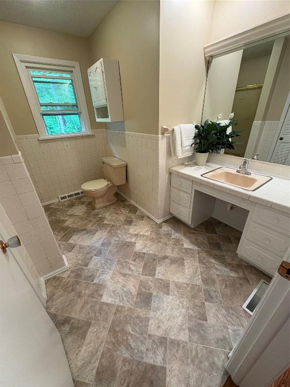 3322 Patio Dr, Millcreek, PA 16506 - full bathroom with tile walls, a wainscoted wall, vanity, toilet, and stone finish flooring