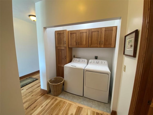 clothes washing area with washer and dryer, cabinets, and light hardwood / wood-style flooring