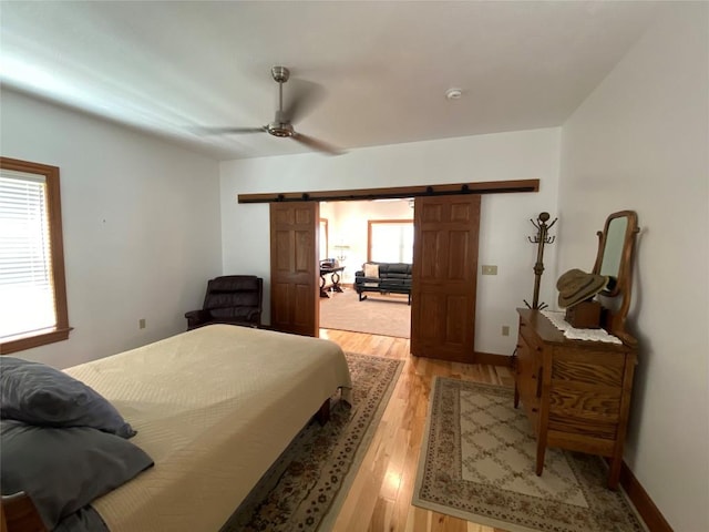 bedroom with ceiling fan, a barn door, and light hardwood / wood-style flooring