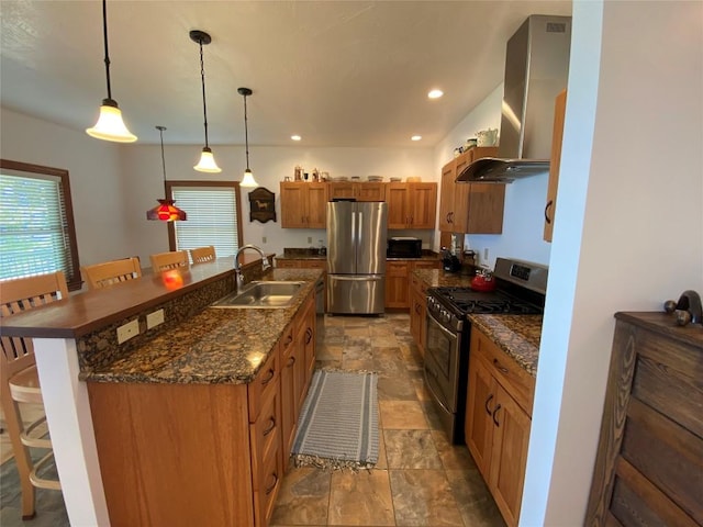 kitchen with a large island, stainless steel appliances, wall chimney range hood, decorative light fixtures, and a breakfast bar area