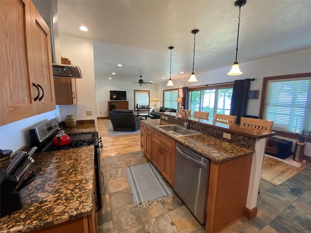 kitchen featuring stainless steel dishwasher, black range oven, a kitchen island with sink, sink, and pendant lighting