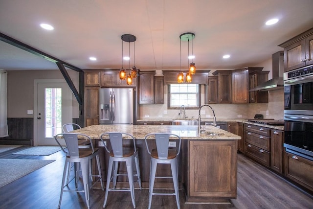 5499 Pinetree Rd, Mckean, PA 16426 - kitchen with stainless steel appliances, wall chimney exhaust hood, light stone counters, an island with sink, and dark wood finished floors
