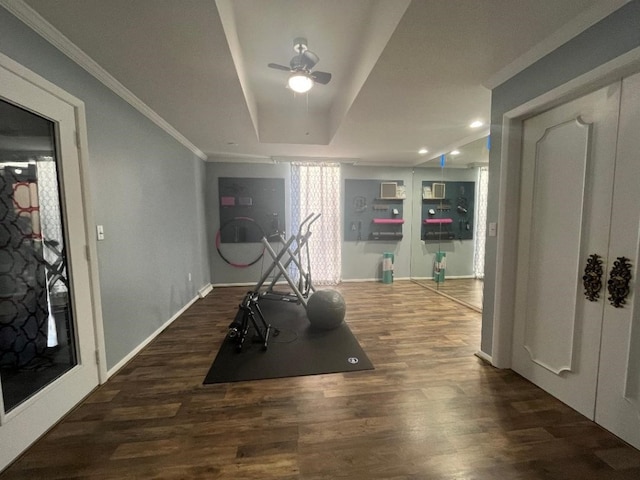 exercise area with a raised ceiling, dark hardwood / wood-style floors, and ornamental molding