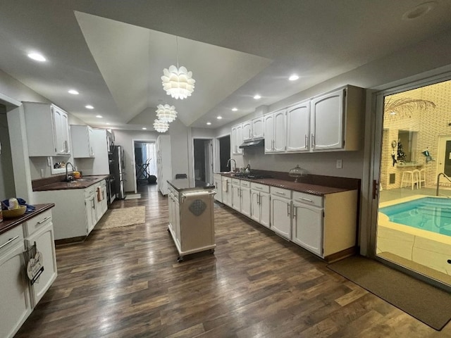 kitchen with vaulted ceiling, sink, white cabinets, dark hardwood / wood-style floors, and hanging light fixtures