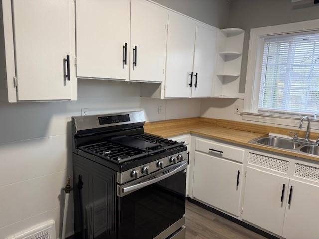kitchen featuring white cabinets, a sink, open shelves, light countertops, and stainless steel gas range oven