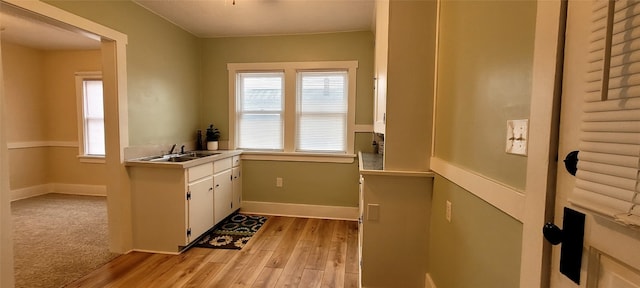 interior space with baseboards, light countertops, light wood-style floors, white cabinetry, and a sink