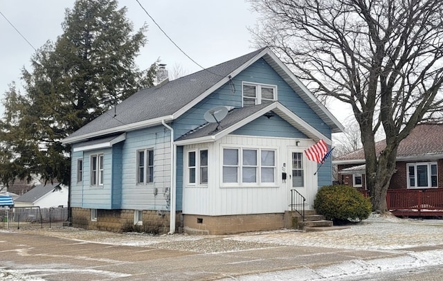 bungalow-style home with entry steps, a shingled roof, a chimney, and fence