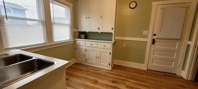 kitchen featuring light wood-style flooring, a sink, white cabinetry, baseboards, and light countertops