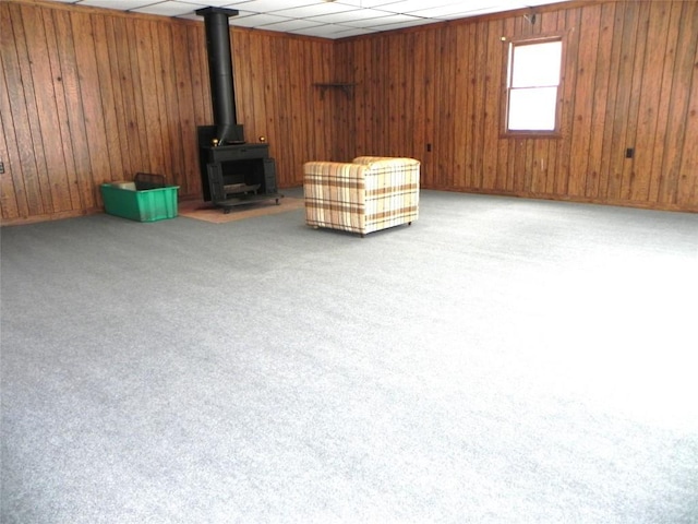 unfurnished room with wood walls, a drop ceiling, a wood stove, and light colored carpet