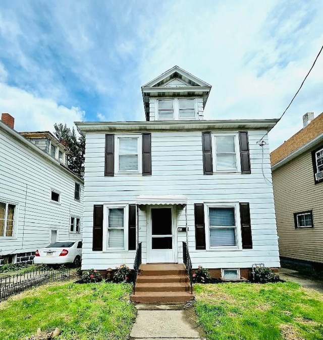 american foursquare style home with entry steps, a front lawn, and fence