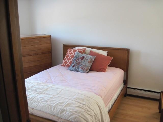 bedroom with light hardwood / wood-style flooring and a baseboard heating unit