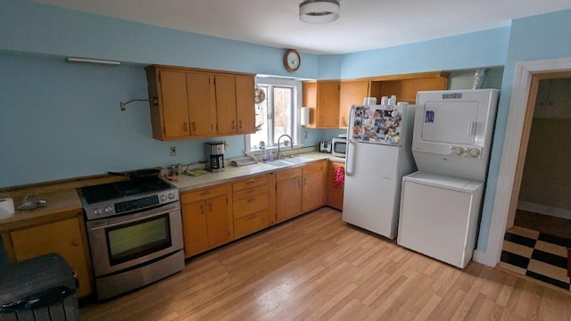 kitchen with sink, stainless steel appliances, stacked washer and clothes dryer, and light wood-type flooring