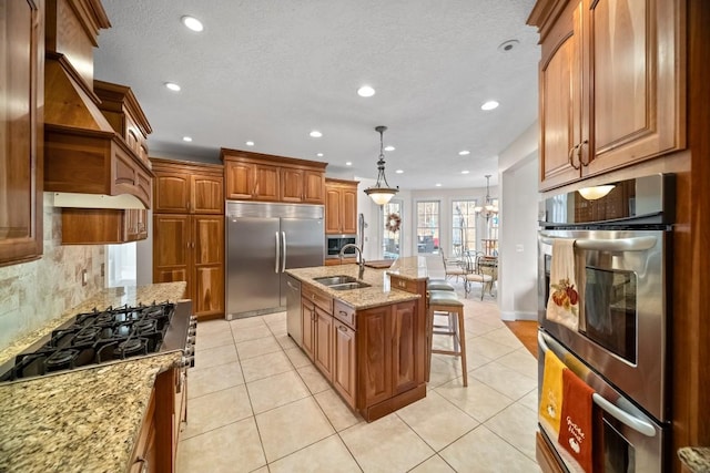 kitchen with a center island with sink, sink, decorative backsplash, appliances with stainless steel finishes, and decorative light fixtures