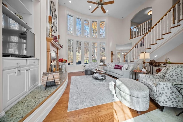 living room with ceiling fan with notable chandelier, a high ceiling, and light wood-type flooring