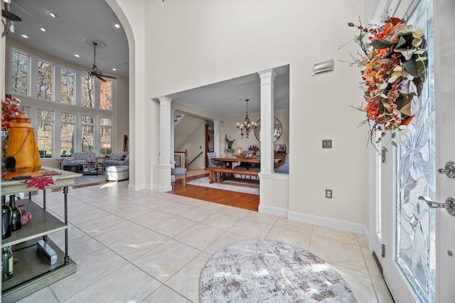 tiled foyer entrance featuring a high ceiling, ceiling fan with notable chandelier, and ornate columns