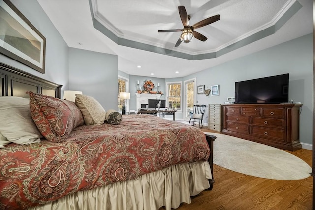 bedroom featuring a raised ceiling, ceiling fan, wood-type flooring, and ornamental molding