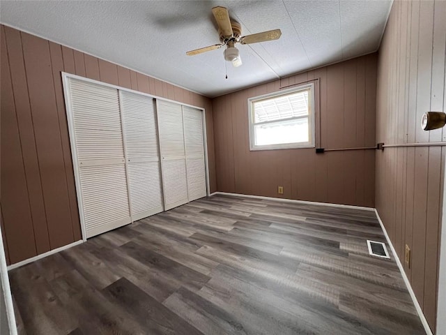 unfurnished bedroom featuring a textured ceiling, ceiling fan, a closet, and wood walls