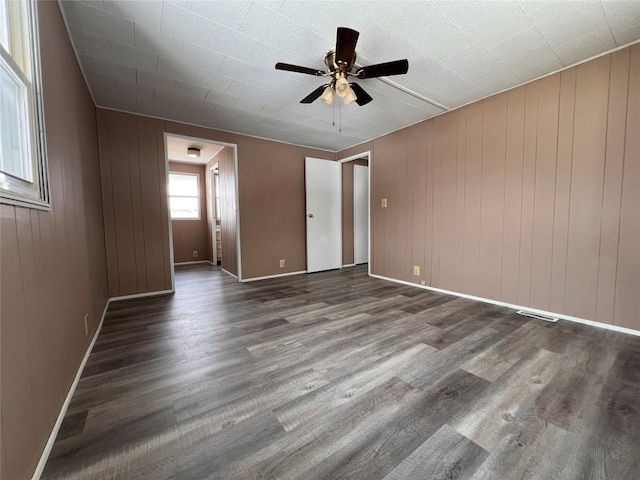 unfurnished bedroom featuring ceiling fan, wood walls, and dark hardwood / wood-style flooring