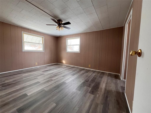 spare room featuring ceiling fan, wood walls, and dark wood-type flooring