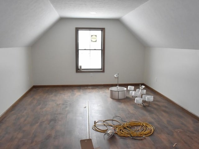 additional living space with vaulted ceiling, a textured ceiling, baseboards, and wood finished floors