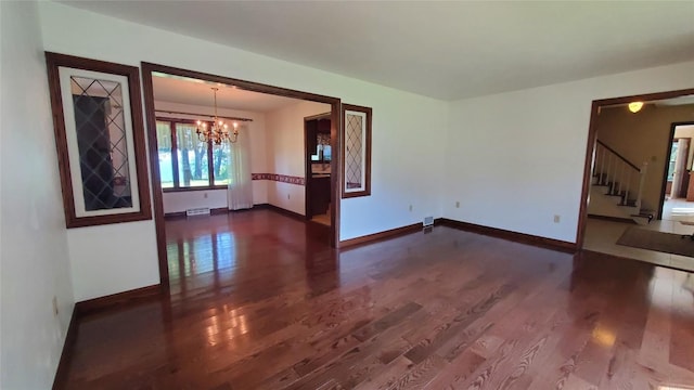 empty room with dark hardwood / wood-style flooring and an inviting chandelier