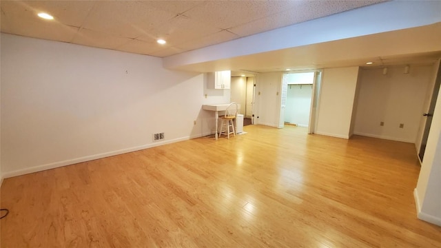 basement featuring a paneled ceiling and light hardwood / wood-style flooring