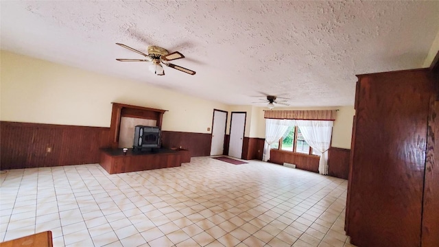 unfurnished living room with a wood stove, ceiling fan, and a textured ceiling