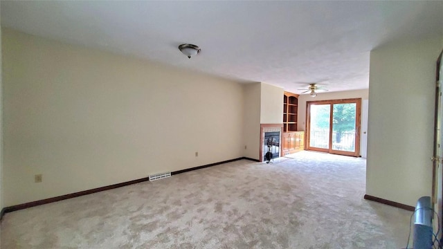 unfurnished living room with built in shelves, ceiling fan, and light carpet