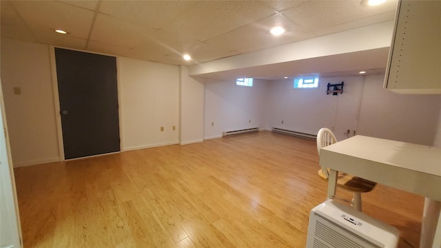 basement featuring baseboard heating, light hardwood / wood-style flooring, and a drop ceiling