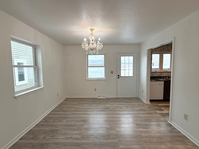 unfurnished dining area with hardwood / wood-style floors, a notable chandelier, and a textured ceiling