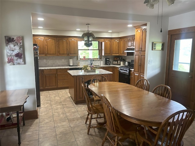 kitchen with hanging light fixtures, black range with gas stovetop, backsplash, a kitchen island, and exhaust hood