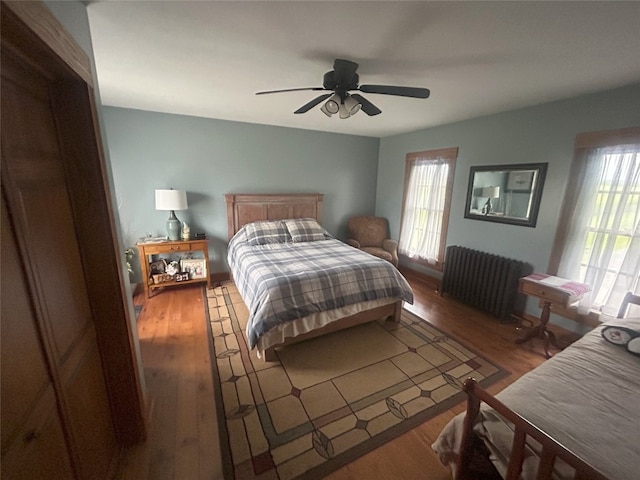 bedroom featuring ceiling fan, radiator heating unit, and dark wood-type flooring