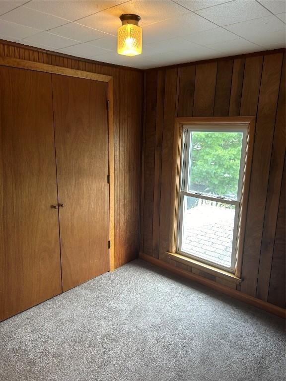 unfurnished bedroom featuring carpet flooring, a closet, and wooden walls