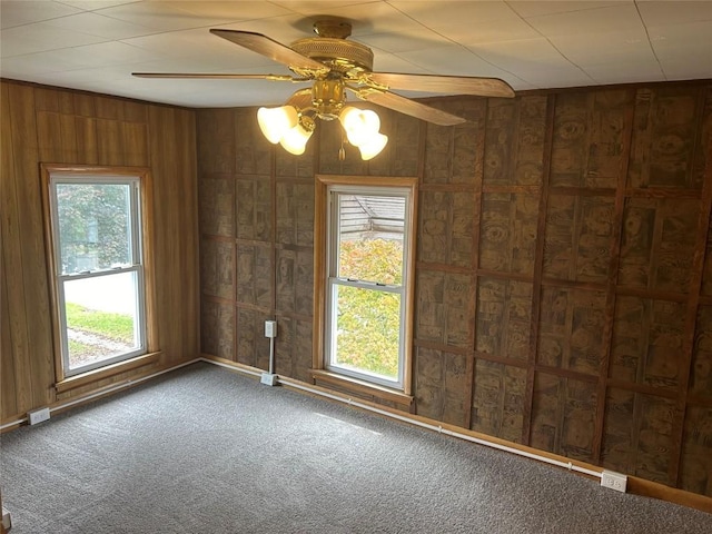 carpeted empty room with ceiling fan and wood walls