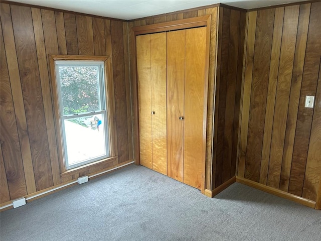 unfurnished bedroom featuring wooden walls, a closet, and light colored carpet